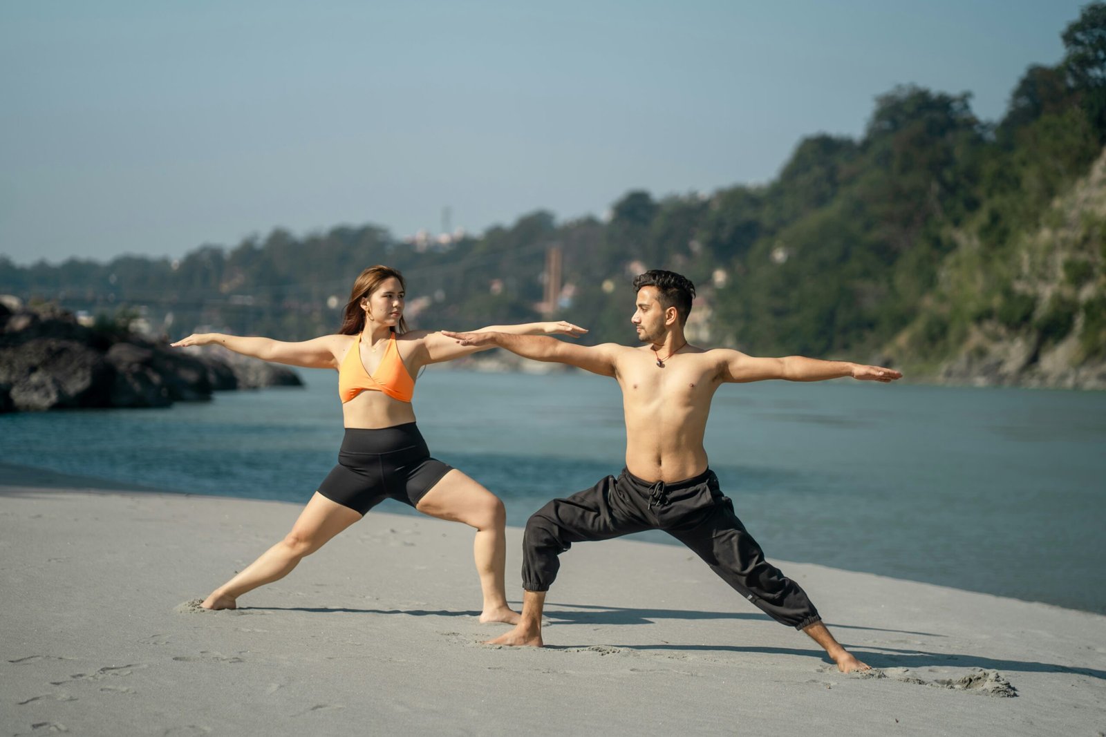 Couple practicing yoga by the river in Rishikesh, capturing the disciplined and energizing mood of peak retreat season in India.