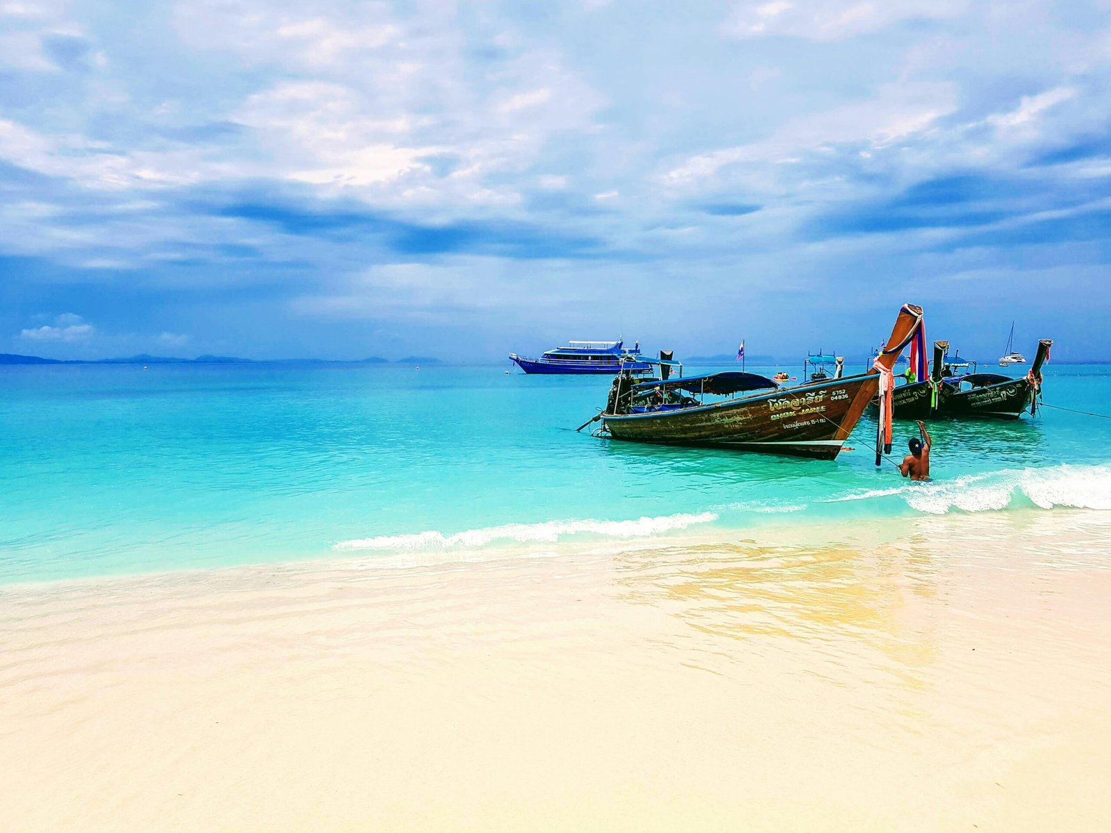 Traditional Thai longtail boats with colorful ceremonial scarves anchored on a turquoise beach in Phuket, Thailand, perfect for a 2026 island-hopping yoga retreat