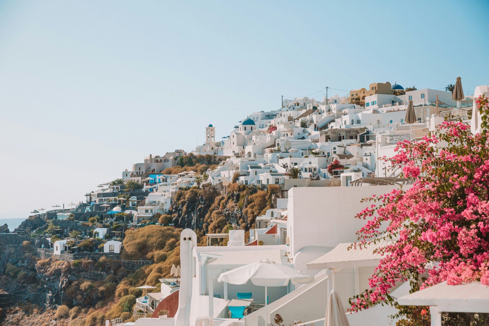 White hillside homes and pink blossoms in Santorini, bringing a fresh island atmosphere to a Greece retreat in May.
