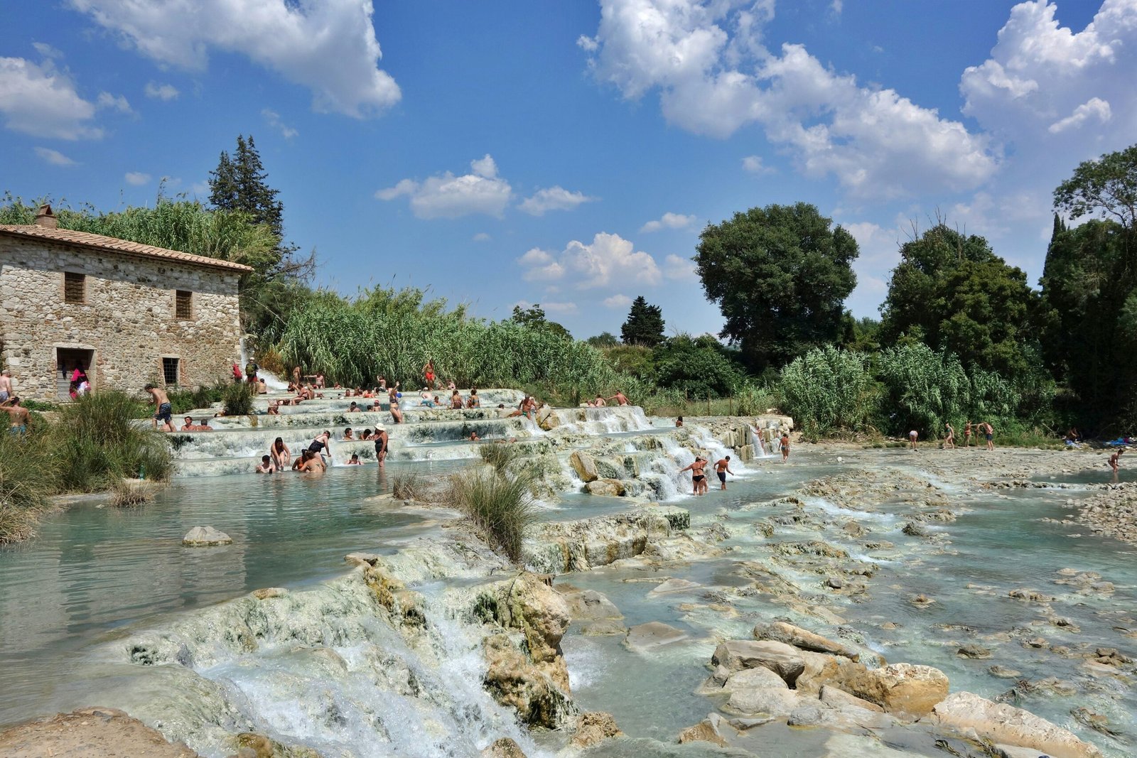People relaxing in natural thermal waters beside a stone building, capturing the soothing and rejuvenating spirit of a retreat escape