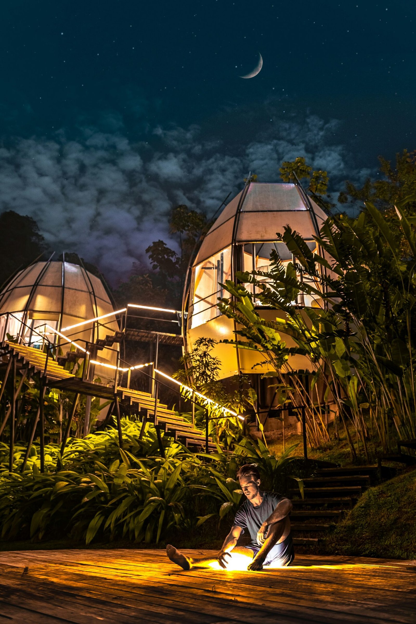 Person seated peacefully outside glass dome retreat pods in a quiet natural setting for rest, reflection, and renewal