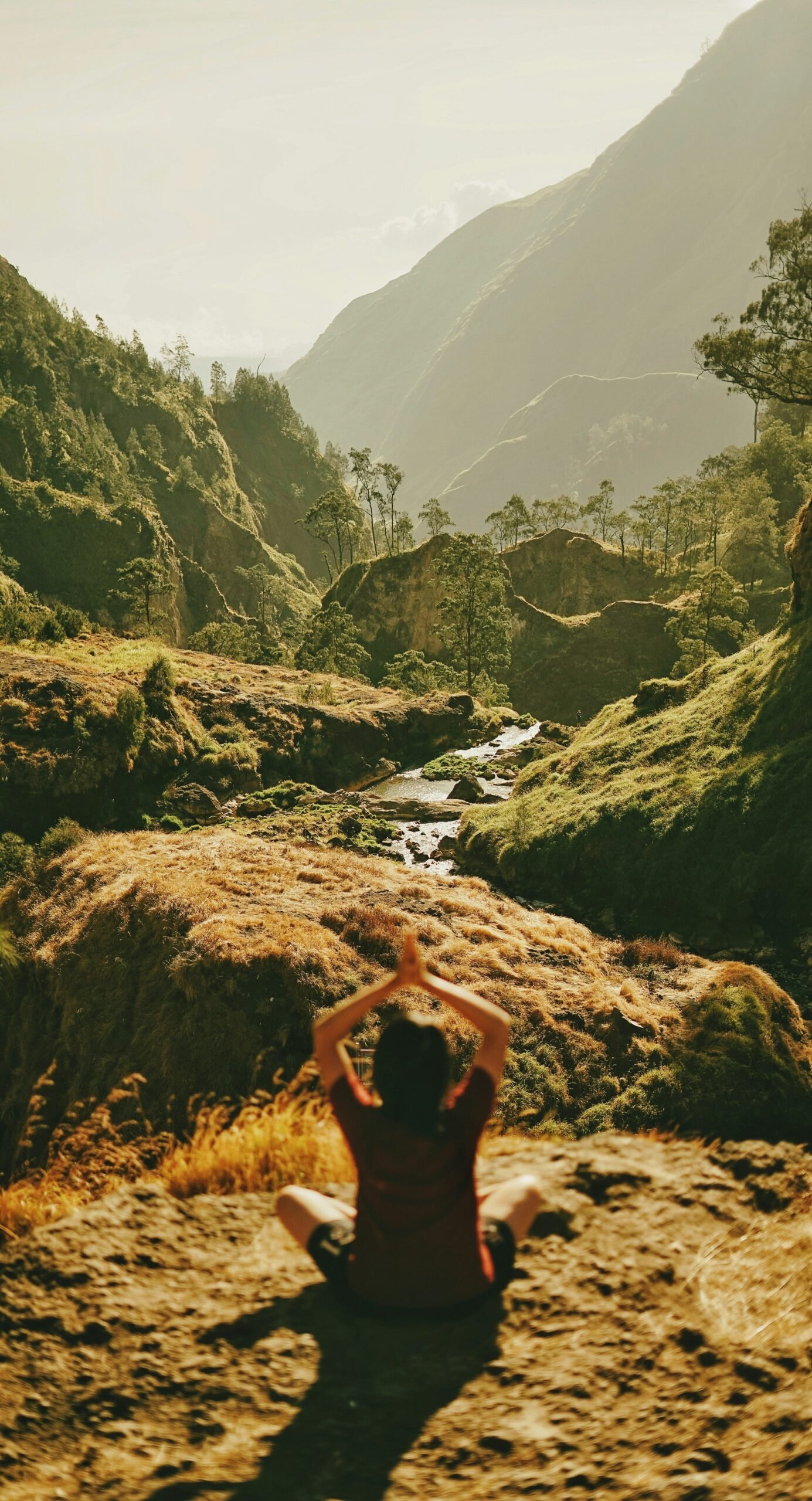 A woman meditating on a rocky peak overlooking a lush, sun-drenched valley, representing the deep connection to nature and sustainable mindfulness found at a Portuguese eco-retreat.